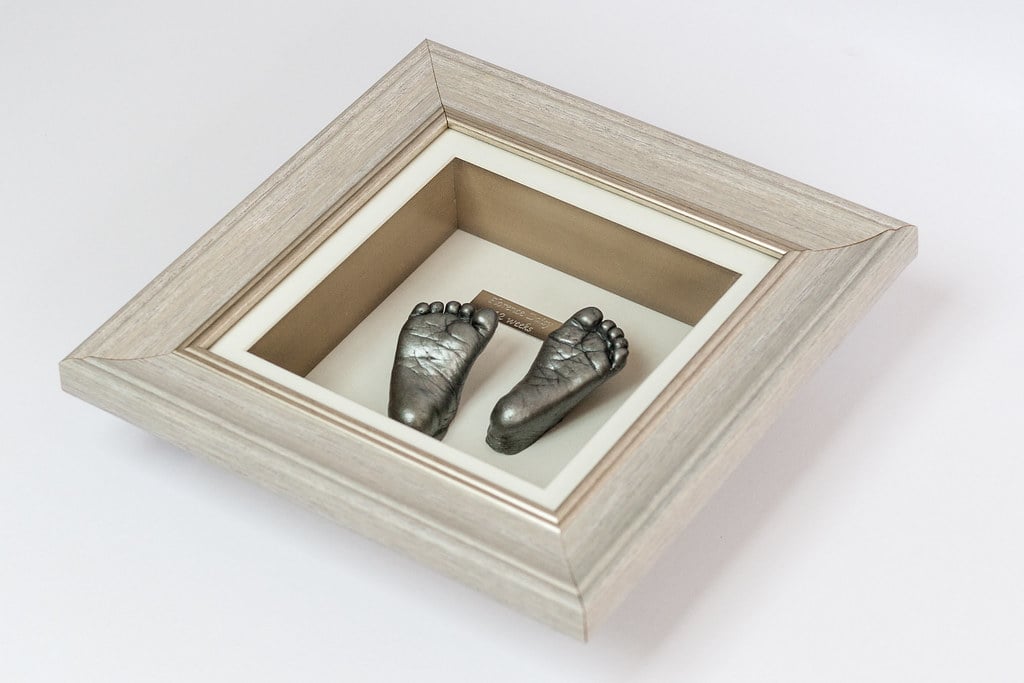 Bronze baby hand and foot casting displayed in decorative frame